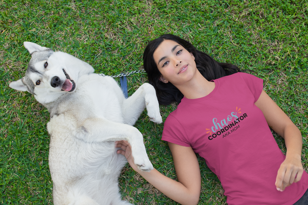 Woman lying on grass with a white dog, wearing a pink t-shirt with text.